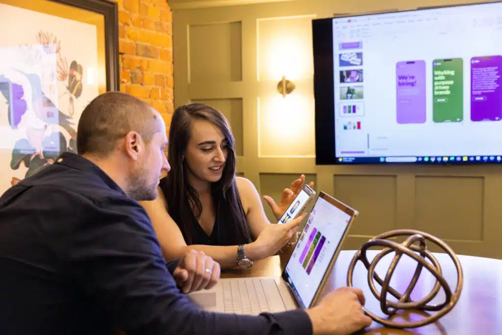 two people working together, one showing something on their phone to the other person