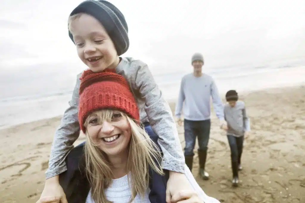Family on beach in winter, mother giving son piggyback