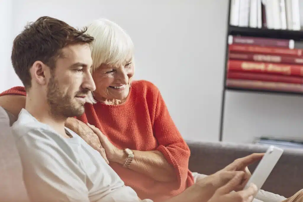 Grandson sitting on couch, using digital tablet with his grandmother