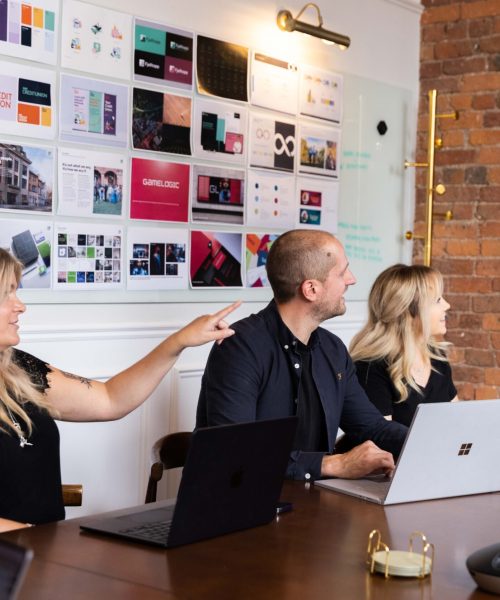 three people working together on a project, looking towards a screen with information on