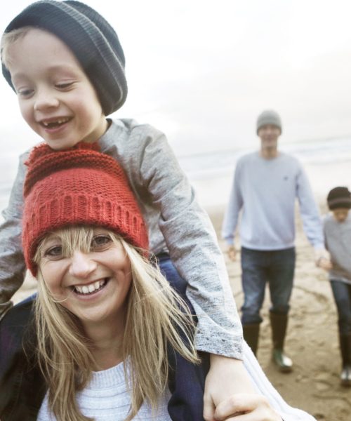 Family on beach in winter, mother giving son piggyback